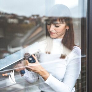 Kobieta aplikująca odrobinę koncentratu płynu do mycia okien za pomocą kulki roll-on bezpośrednio na myjkę do szyb, przygotowując ją do skutecznego i bezsmugowego czyszczenia powierzchni szklanych.